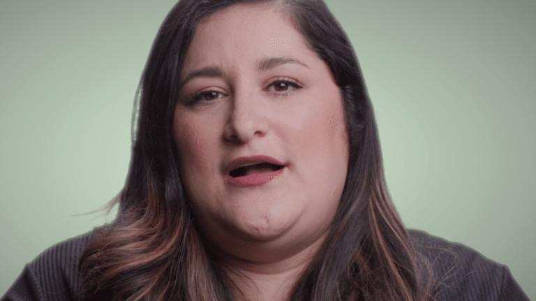 Woman with long dark hair speaks against a light green background.