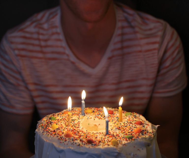 A person wearing a striped shirt blows out candles on a birthday cake decorated with sprinkles and colorful candies.