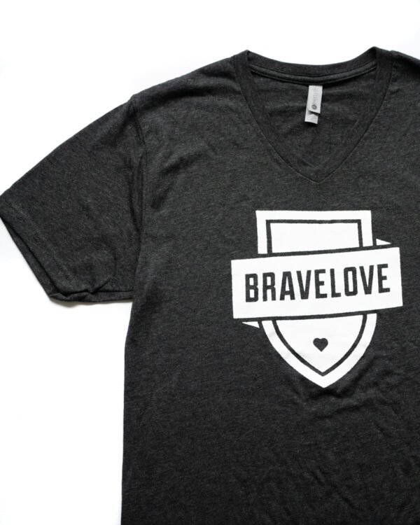 Black V-neck t-shirt featuring a white shield design with the word "BRAVELOVE" printed in bold letters, completed with a small heart at the bottom.