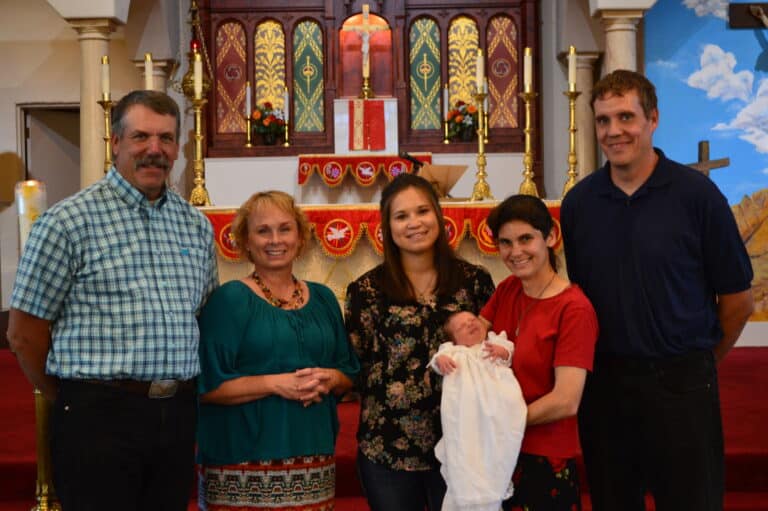 A group of six people, including a baby in a white outfit, posing in front of an ornate church altar.