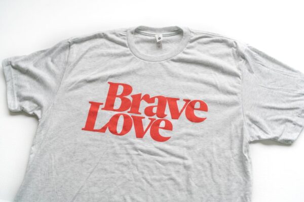 Introducing the New! BraveLove T-Shirt: a stylish gray tee featuring bold red text that reads "Brave Love," showcased on a pristine white background.