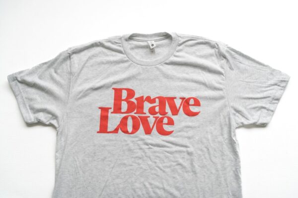 A New! BraveLove T-Shirt in grey, featuring the text "Brave Love" printed in bold red letters on the front.