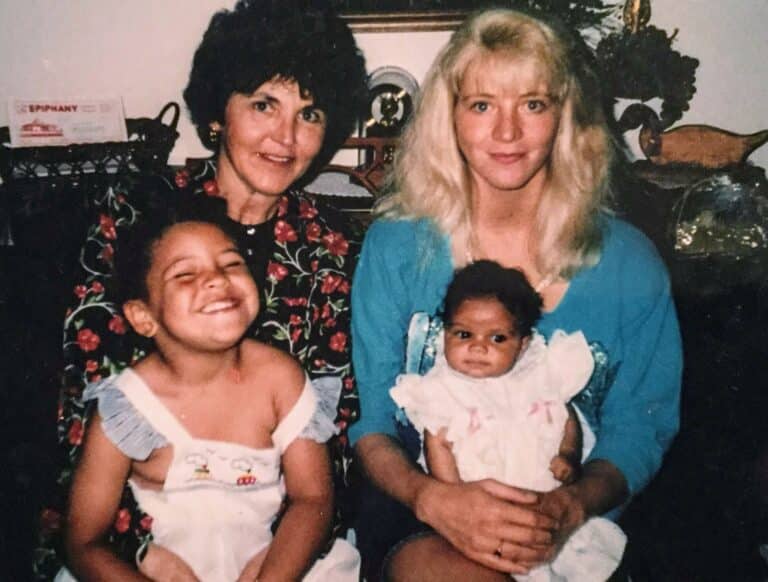 Two women sit side by side. One woman has two children on her lap, an older child smiling broadly and a baby looking at the camera.