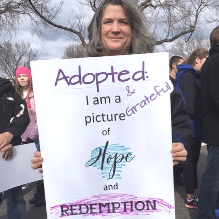 A person holding a sign that reads, "Adopted: I am a picture of hope and redemption & grateful," during a rally.