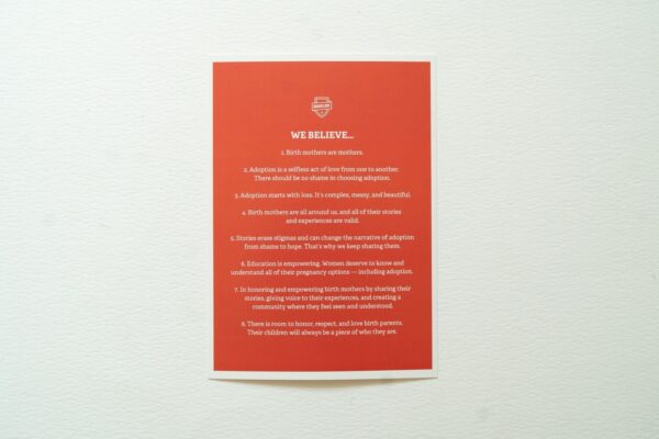 A Manifesto Card titled "We Believe..." in red, featuring 8 statements about adoption and birth mothers, is pinned to a light gray surface.