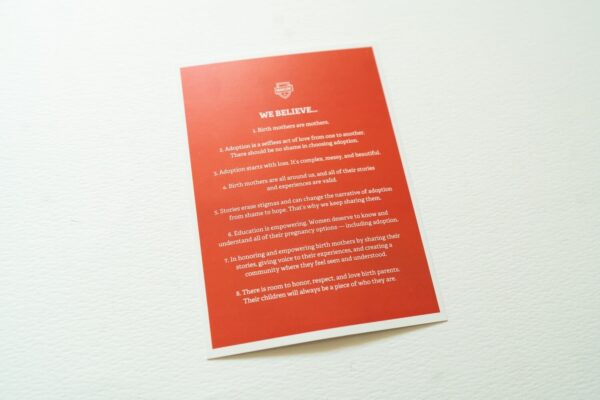 A Manifesto Card with white text outlining beliefs about adoption, motherhood, birth mothers, and education, placed on a white surface.