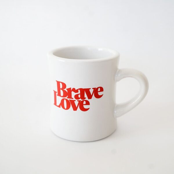 A "New! BraveLove Mug" featuring a white ceramic finish and a bold red "Brave Love" print, displayed against a plain white background.