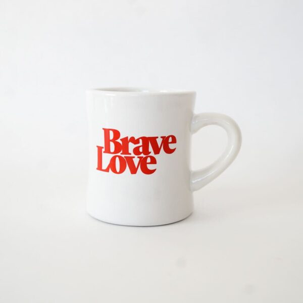 Introducing the latest New! BraveLove Mug - a pristine white mug adorned with bold red "Brave Love" text, elegantly set against its plain white surface.