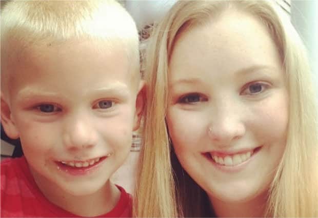 A young woman and a boy with blond hair smiling at the camera. The boy is wearing a red shirt.