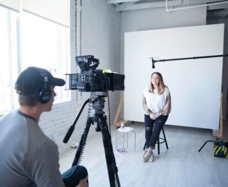 A woman being interviewed on camera in a bright studio; a man operates the camera.