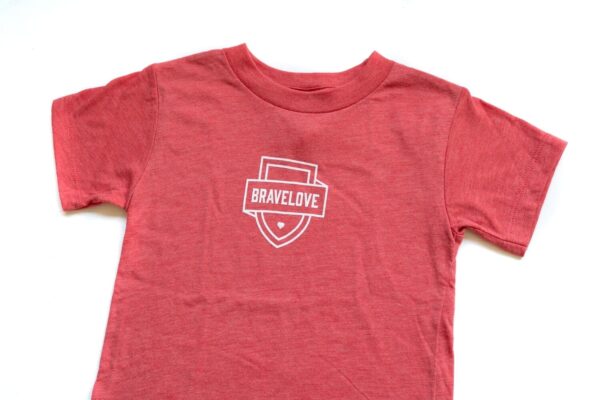 Toddler T-Shirt in red featuring a white "BRAVELOVE" logo and shield graphic on the chest, showcased against a white background.