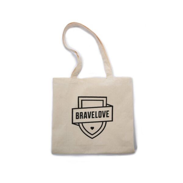 A beige tote bag with a long handle, featuring a black "BRAVELOVE" logo and a shield design with a small heart at the bottom.