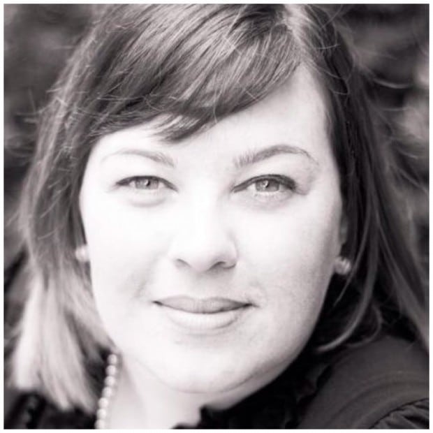 Black and white close-up portrait of a person with short, dark hair, wearing a necklace and looking directly at the camera with a slight smile.