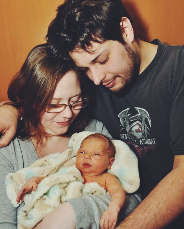 A man and woman lovingly gaze at the newborn baby they hold, wrapped in a soft, patterned blanket.