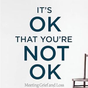 Text reads "It's OK That You're Not OK" with "Meeting Grief and Loss" below. An empty chair is partially visible on the right.